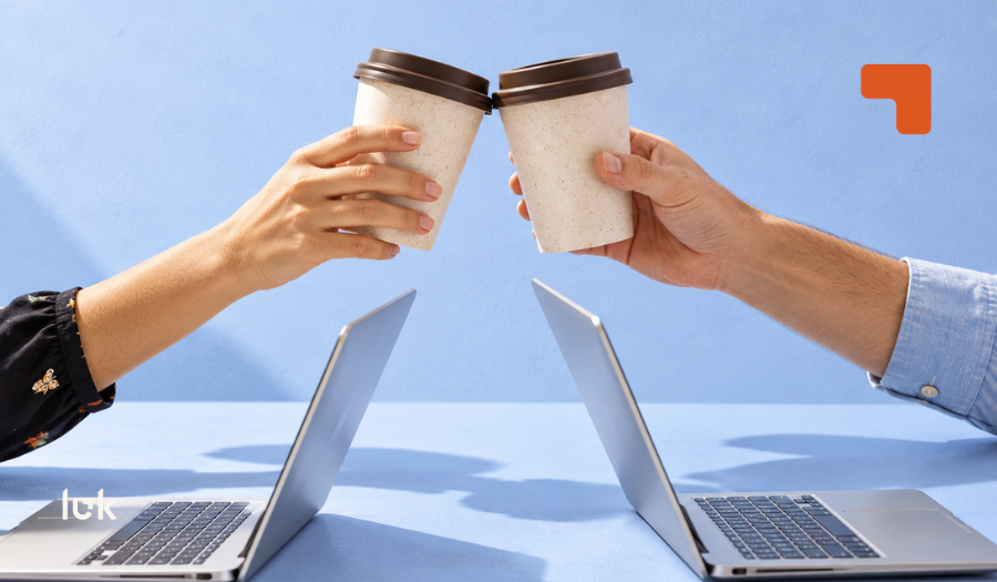 Dos personas chocando vasos de café sobre una mesa con dos computadores